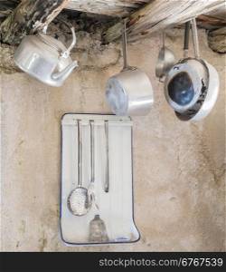 Old kitchen utensils in aluminum. Hanging from old wooden beams, pans, strainer, kettle