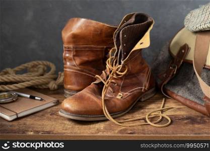 old leather travel vintage boots shoes and bag at wooden table, with wall background texture