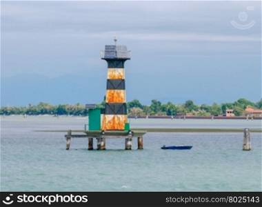 Old lighthouse in the middle of the Venetian lagoon. The lagoon is very busy shipping.. Venice. Old lighthouse.