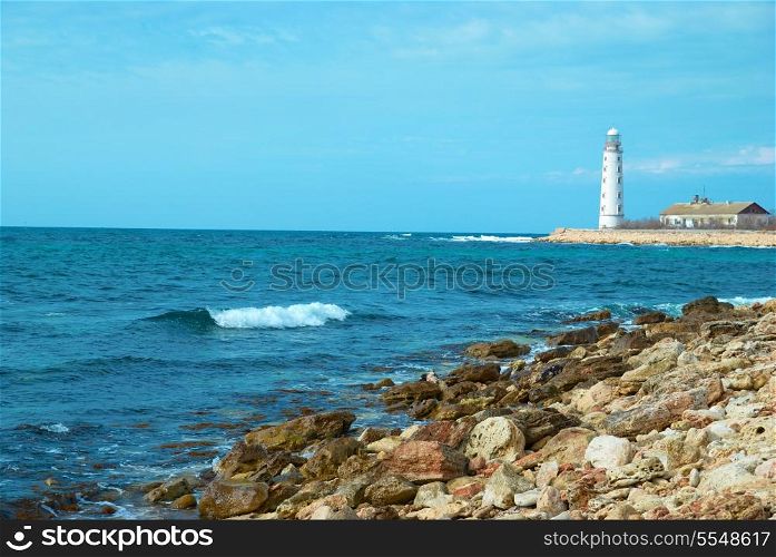 Old lighthouse on the sea coast. Storm, waves and blue sky.