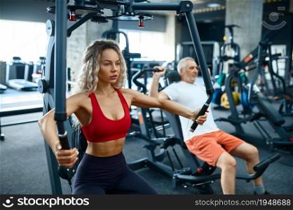 Old man and female personal trainer on exercise machines, gym interior on background. Sportive grandpa with woman instructor, training in sport center. Healty lifestyle, health care. Old man and female trainer on exercise machines