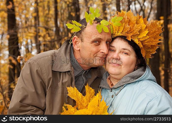 Old man and old woman with wreath of maple leaves embrace in autumnal forest