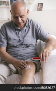 Old man applying ointment on knee