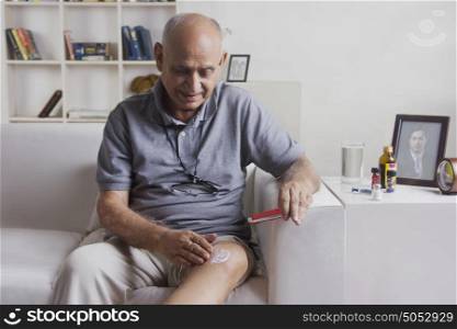 Old man applying ointment on knee