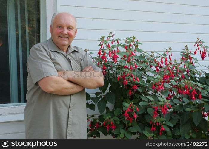 Old man - grower of flowers next to flower bush in summer day.