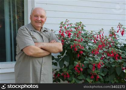 Old man - grower of flowers next to flower bush in summer day.