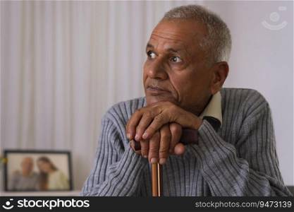 Old man looking away while sitting with leaning on walking stick