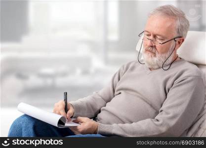 Old man making a shopping list with a pen on paper for holidays