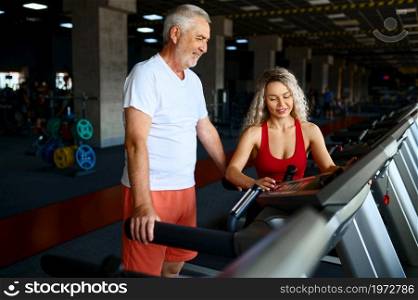 Old man on treadmill, female personal trainer, gym interior on background. Sportive grandpa with woman instructor in sport center. Healty lifestyle, health care. Old man on treadmill, female personal trainer