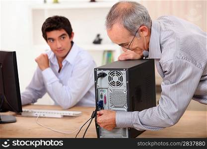 old man plugs a computer under the watch of a young man