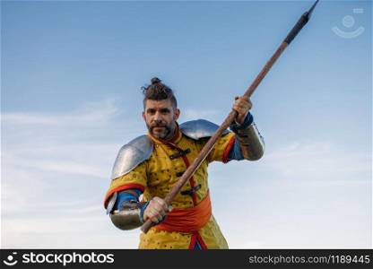 Old medieval knight in armor holds axe, great tournament. Armored ancient warrior in armour posing in the field. Old medieval knight in armor holds axe
