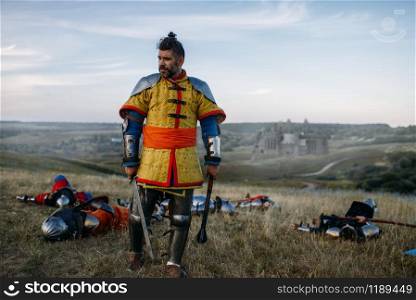 Old medieval knight in armor looks at the dead after great battle. Armored ancient warrior in armour posing in the field