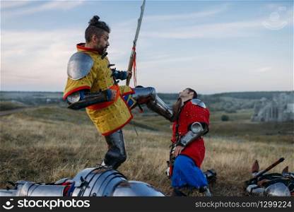 Old medieval knight in armor prepares to cut off head, great battle. Armored ancient warrior in armour posing in the field. Medieval knight in armor prepares to cut off head