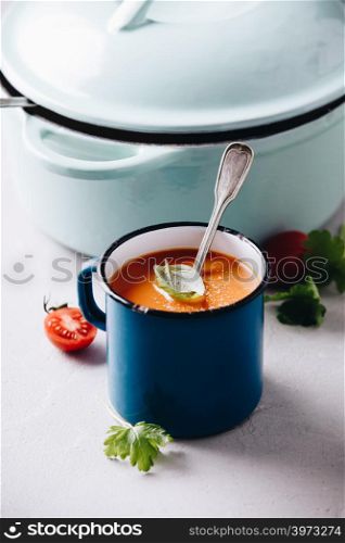 Old metal cup of tomato soup and cooking pot on concrete background, close up
