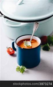 Old metal cup of tomato soup and cooking pot on concrete background, close up