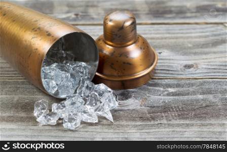 Old metal drink mixer lying on side with crushed ice flowing out onto rustic wood