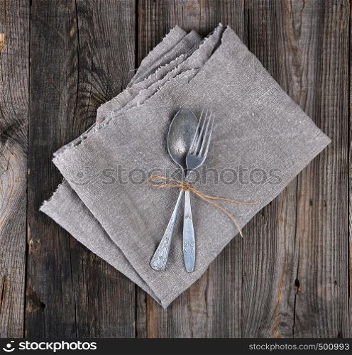 old metal fork and spoon tied with a brown rope on a gray linen napkin, instruments are crossed