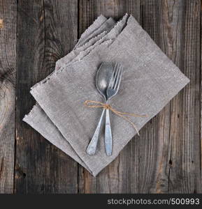 old metal fork and spoon tied with a brown rope on a gray linen napkin, instruments are crossed
