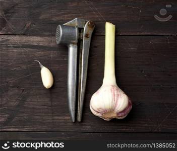 old metal garlic press and fresh young white garlic on a brown wooden table, top view
