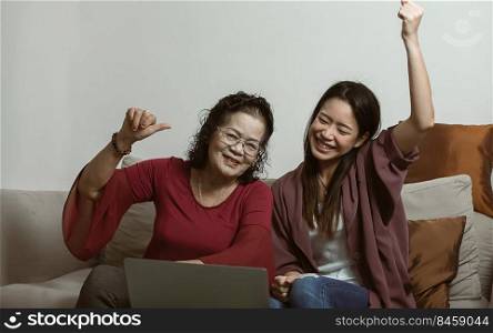 Old mother and young dauthter are happy while using laptop at home. Aging people and Technology Concept.