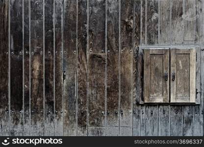 Old neglected rustic shutters closed on aging wooden wall