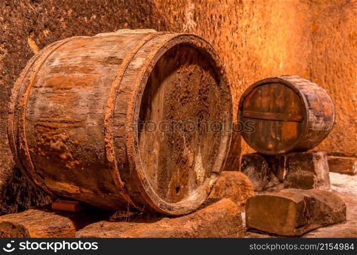 Old oak barrel with rusty hoops. Deep wine cellar with textured walls. Old Wine Cellar and Barrels
