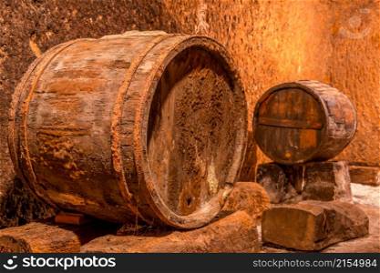 Old oak barrel with rusty hoops. Deep wine cellar with textured walls. Old Wine Cellar and Barrels