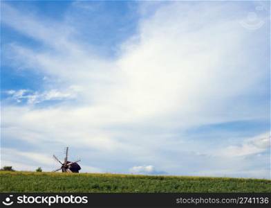 Old obsolete windmill beyond the hill on field
