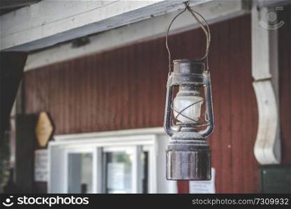 Old oil lamp hanging on a porch outside a red house in old style