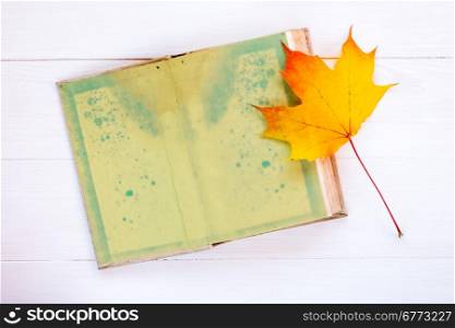 Old open book and autumn maple leaf on white planks background