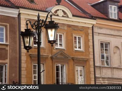 Old ornate lanterns in front of the orange facades of old buildings in Warsaw Poland