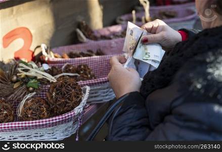 old pensioner woman putting money (euros) out of her purse and is paying paying something on a market, woman falling for a fraud and spending money
