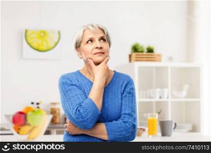 old people and decision making concept - portrait of senior woman in blue sweater thinking over kitchen background. portrait of senior woman thinking in kitchen