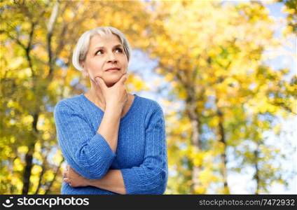 old people and decision making concept - portrait of senior woman in blue sweater thinking over autumn park background. portrait of senior woman thinking in autumn park