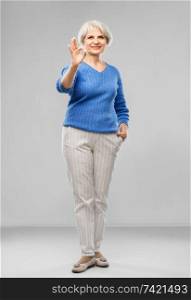 old people concept - portrait of smiling senior woman in blue sweater making ok gesture over grey background. portrait of smiling senior woman making ok gesture
