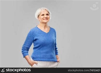 old people concept - portrait of smiling senior woman in blue sweater over grey background. portrait of smiling senior woman in blue sweater