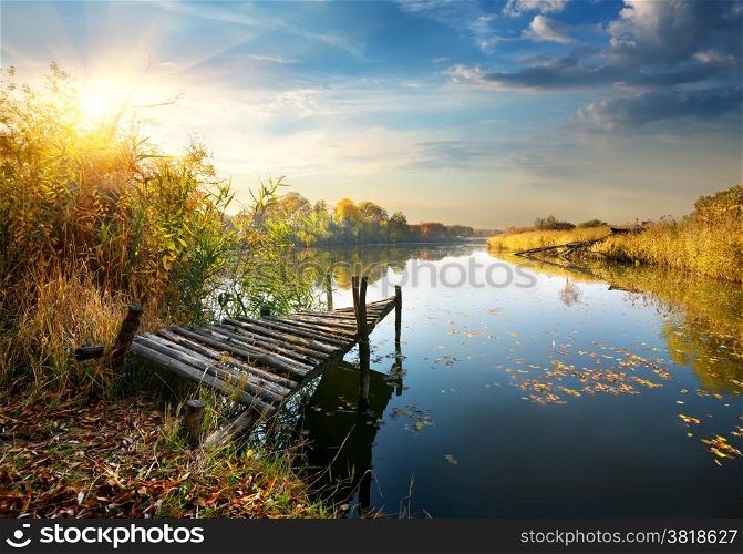 Old pier on autumn river at sunset