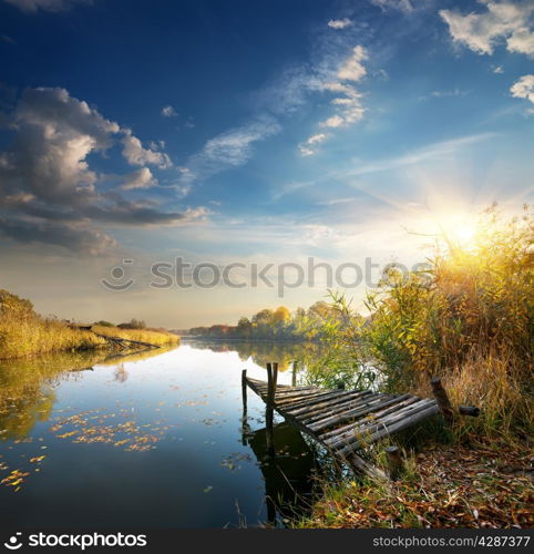Old pier on autumn river at sunset