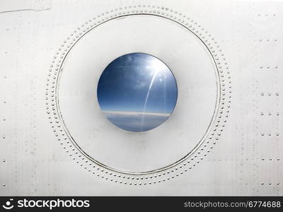 OLd Porthole of an jet airplane with a sunny sky