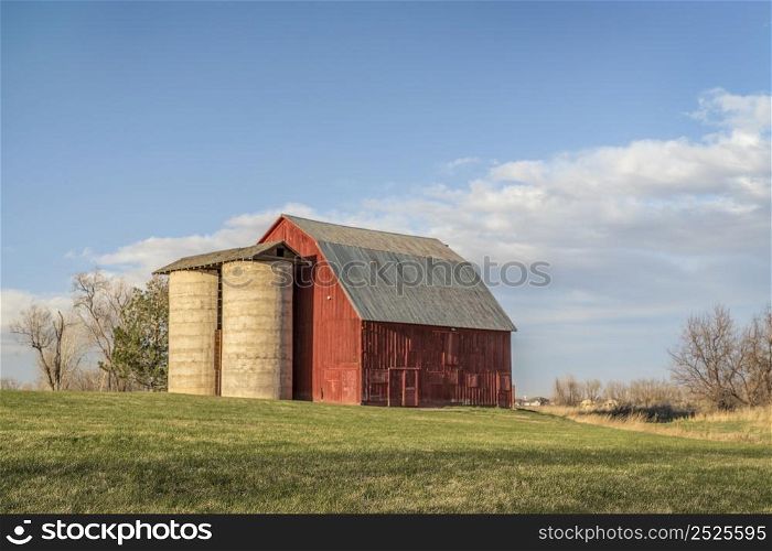 old red barn with twin silo and irrigation ditch at Colorado foothills, early spring scenery at sunset, public Shenandoah Park in Fort Collins