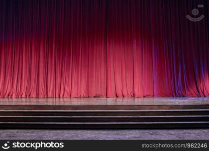 Old red curtains on a stage with lights in the front of the stage.