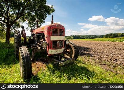 Old red rusty tractor in a field. Sunny summer day. Copy space. Old red rusty tractor in a field