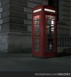 old red telephone booth at night in london on pavement near old building