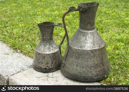 Old retro metal traditional vessels on stone and green grass
