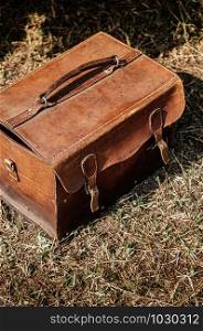 Old retro vintage leather picnic bag with dull surface and scratch on grass lawn under sun, close up details