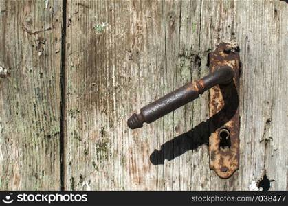 Old retro vintage rusty iron door handle and keyhole closeup on weathered grunge wooden board surface