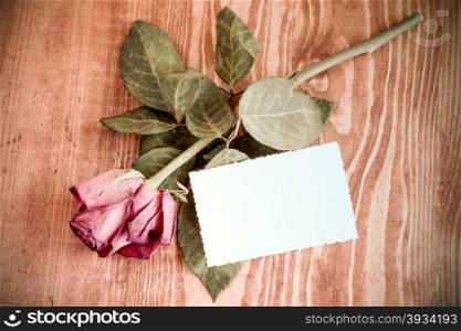 Old rose and blank greeting card over wooden table. Top view with copy space
