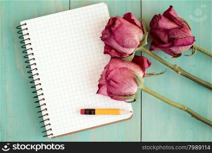 Old roses and blank notebook over wooden table. Top view with copy space.