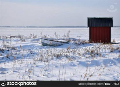 Old rowing boat by a red fishing cabin in winter season