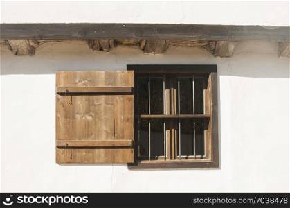 Old rural brown wooden window with open shutter on white country house wall